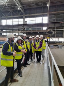 Nine people wearing high visibility jackets and hard hats stand together in an industrial setting during a visit to Drax power station