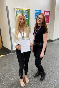 Inside our Hub campus, student Freya poses with a certificate next to a member of staff