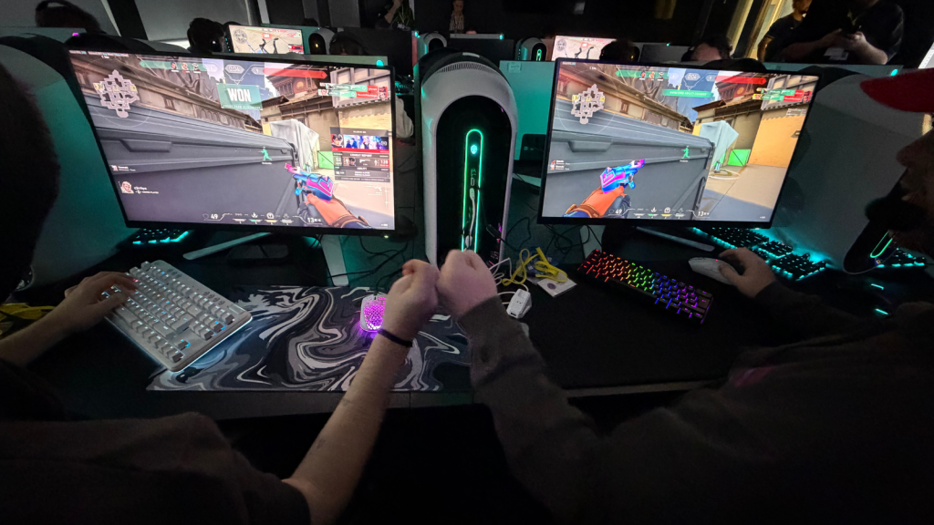 Alt text: Two students compete in an esports match during the Inter-College Championships 2026, seated at side-by-side gaming PCs with illuminated keyboards and large monitors displaying a first-person shooter game in a darkened gaming arena. 